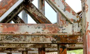 Metalowa konstrukcja z widoczną, postępującą korozją. Rdza i łuszcząca się farba tworzą mozaikę na belkach i słupach.