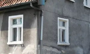 Szare ściany domu z białymi, tradycyjnymi okna skrzynkowe. Dach pokryty czerwona dachówką.