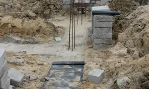 Budowa domu w toku. Widać wykopy, zbrojenie i materiały budowlane. Fundament czeka na zalanie.