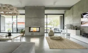 Nowoczesny salon z kominkiem obłożonym betonem architektonicznym. Podłoga i ściany również wykonane z mikrobetonu, tworząc spójną, minimalistyczną przestrzeń.