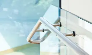 Nowoczesne mocowanie balustrady od czoła do szklanej tafli. Metalowy uchwyt pewnie trzyma się szkła, zapewniając bezpieczeństwo.