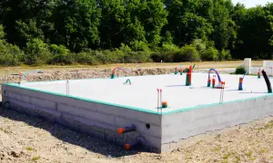 Nowa płyta fundamentowa z wystającymi rurami i instalacjami, gotowa na dalsze prace budowlane.