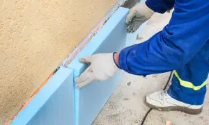 Ręce w rękawiczkach układają niebieski styropian na fundamencie. To kluczowy etap budowy, by wybrać odpowiedni styropian na fundament.