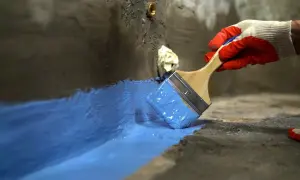 Rękawica w czerwonej rękawicy nakłada niebieski szlam hydroizolacyjny na betonową powierzchnię, tworząc barierę ochronną.