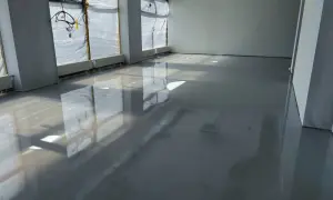 Lśniąca podłoga z żywicy w pomieszczeniu w budowie. Widać odbicia okien i instalacji.