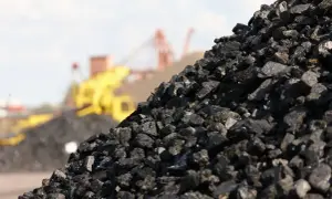 Góra węgla na składzie, maszyny przemysłowe w tle. Obrazek ilustruje aktualną cenę węgla na składach.