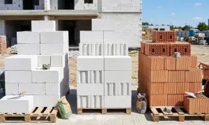 Różne rodzaje pustaków na budowie: białe gazobetonowe i czerwone ceramiczne. W tle budynek w budowie.