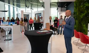 Mężczyzna w garniturze przemawia do grupy osób w nowoczesnym salonie okien i drzwi.