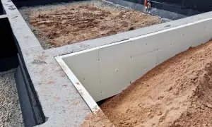 Budowa domu w toku: betonowe stopy fundamentowe, izolacja ze styropianu i nasypy ziemi.