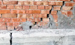 Uszkodzona ceglana ściana z pękniętym betonowym fundamentem.