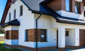 Nowoczesny dom z białym tynkiem, drewnianymi akcentami i kamiennym cokołem na elewacji.