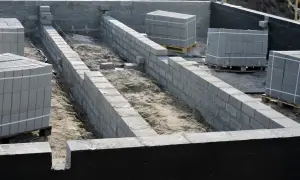 Budowa fundamentów z bloczków betonowych, widoczna izolacja pozioma fundamentów. Materiały budowlane czekają na użycie.