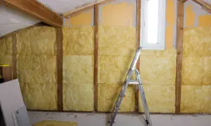 Ocieplenie ścian od wewnątrz wełną mineralną. Widać drewniane belki konstrukcyjne, okno i drabinę.
