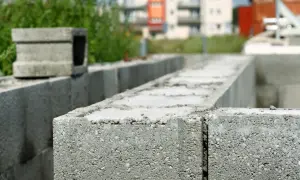 Szary betonowy bloczek zalewowy na budowie, w tle budynki i zieleń.