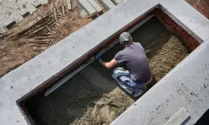 Budowlaniec wyrównuje podsypkę piaskową w wykopie fundamentowym.