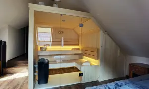 Nowoczesna sauna w domu, wykonana z jasnego drewna, z przeszklonymi drzwiami i nastrojowym oświetleniem. Idealne miejsce na relaks.