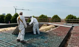 Dwóch pracowników w kombinezonach ochronnych usuwa eternit z dachu. Kiedyś popularny materiał budowlany, dziś wymaga specjalistycznej utylizacji.