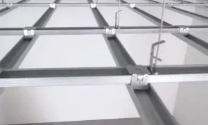 Sufit podwieszany krzyżowy z białymi panelami i metalową konstrukcją. Widać system profili, który tworzy siatkę, a nie pojedyncze belki.