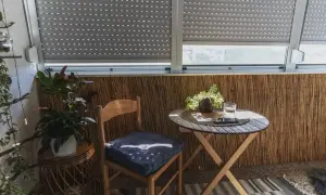 Drewniane krzesło i stolik na balkonie z roletami i roślinami.