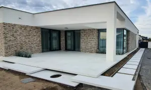 Nowoczesny dom z ceglaną elewacją i tarasem z jasnego, **betonu szczotkowanego**.