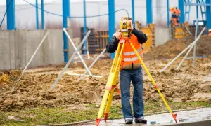 Na budowie technik geodeta w kamizelce odblaskowej mierzy teren za pomocą niwelatora.