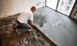 Budowlaniec wyrównuje świeżą wylewkę anhydrytową na podłodze, używając łaty.