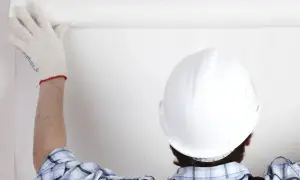 Osoba w kasku i rękawicy przykleja tapetę.