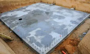 Plac budowy z betonową płytą fundamentową, otoczoną zbrojeniem. To początek budowy ciepłej płyty fundamentowej, która zapewni stabilność i izolację.