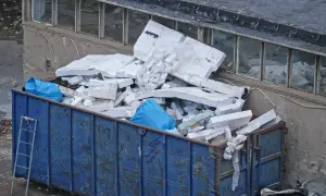 Duży niebieski kontener z gruzem, w tym białym styropianem i niebieskimi workami.