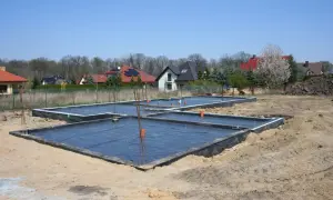 Fundament płyty fundamentowej w budowie, z czarną folią i zbrojeniem.