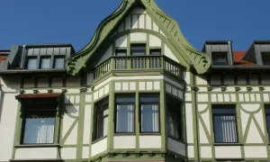 Elegancki ryzalit co to? Wystający fragment fasady budynku, ozdobiony zielonymi elementami i balkonem, z charakterystyczną, falistą formą dachu.