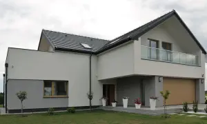Nowoczesny dom z dwuspadowym dachem i balkonem. Elewacja w odcieniach bieli i szarości, z drewnianą bramą garażową. Świetny pomysł na elewację domu.