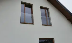 Dwa okna z drewnianymi ramami i szklanymi balustradami na białej ścianie domu.