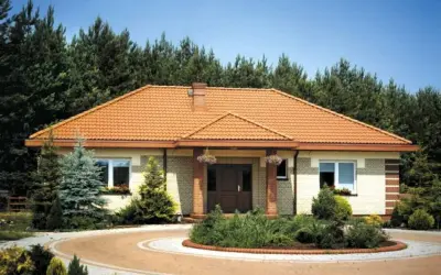 Zabudowany ganek przed domem z pomarańczowym dachem, otoczony zielenią i krętym podjazdem.