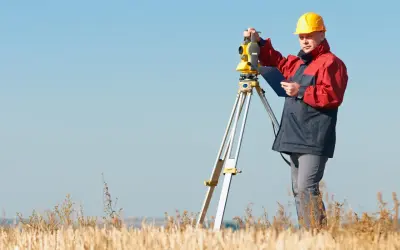 Geodeta w żółtym kasku pracuje z tachimetrem w polu. Zastanawiasz się, ile kosztuje geodeta?