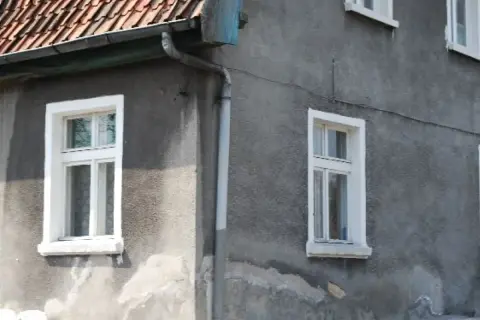 Szare ściany domu z białymi, tradycyjnymi okna skrzynkowe. Dach pokryty czerwona dachówką.