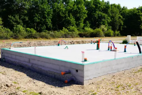 Nowa płyta fundamentowa z wystającymi rurami i instalacjami, gotowa na dalsze prace budowlane.