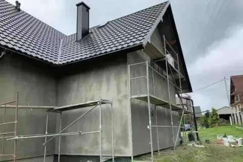 Dom w trakcie prac elewacyjnych, rusztowania wokół, szara ściana. Sprawdzamy elewacja cena za m2 robocizna.