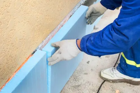 Ręce w rękawiczkach układają niebieski styropian na fundamencie. To kluczowy etap budowy, by wybrać odpowiedni styropian na fundament.
