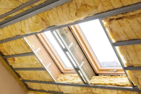 Ocieplenie poddasza wełną mineralną w trakcie prac. Widoczne profile metalowe, wełna i okna dachowe.