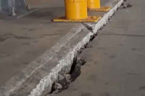 Pęknięcie w betonowej posadzce z widocznymi podporami przemysłowymi w tle.