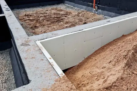 Budowa domu w toku: betonowe stopy fundamentowe, izolacja ze styropianu i nasypy ziemi.