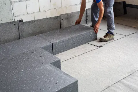 Budowlaniec układa płyty styrobetonu na dachu.