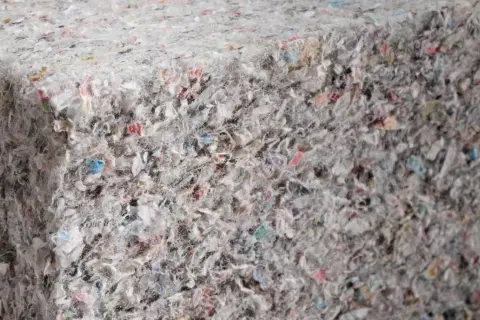 Materiały budowlane: celuloza ocieplenie z recyklingu, tworzące zwartą, włóknistą strukturę z kolorowymi fragmentami.