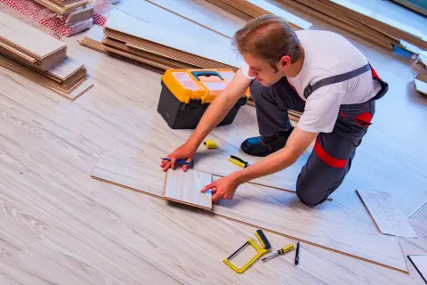 Fachowiec układa panele, planując układanie paneli. Cena usługi zależy od metrażu i trudności. Narzędzia i materiały w pobliżu.