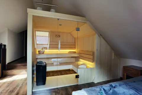 Nowoczesna sauna w domu, wykonana z jasnego drewna, z przeszklonymi drzwiami i nastrojowym oświetleniem. Idealne miejsce na relaks.