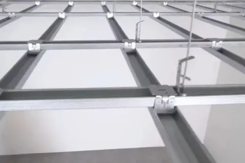 Sufit podwieszany krzyżowy z białymi panelami i metalową konstrukcją. Widać system profili, który tworzy siatkę, a nie pojedyncze belki.