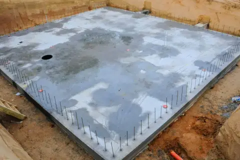 Plac budowy z betonową płytą fundamentową, otoczoną zbrojeniem. To początek budowy ciepłej płyty fundamentowej, która zapewni stabilność i izolację.