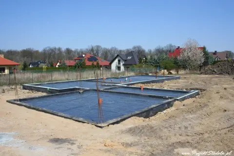 Fundament płyty fundamentowej w budowie, z czarną folią i zbrojeniem.