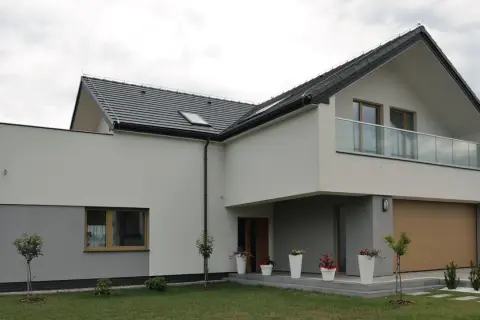 Nowoczesny dom z dwuspadowym dachem i balkonem. Elewacja w odcieniach bieli i szarości, z drewnianą bramą garażową. Świetny pomysł na elewację domu.